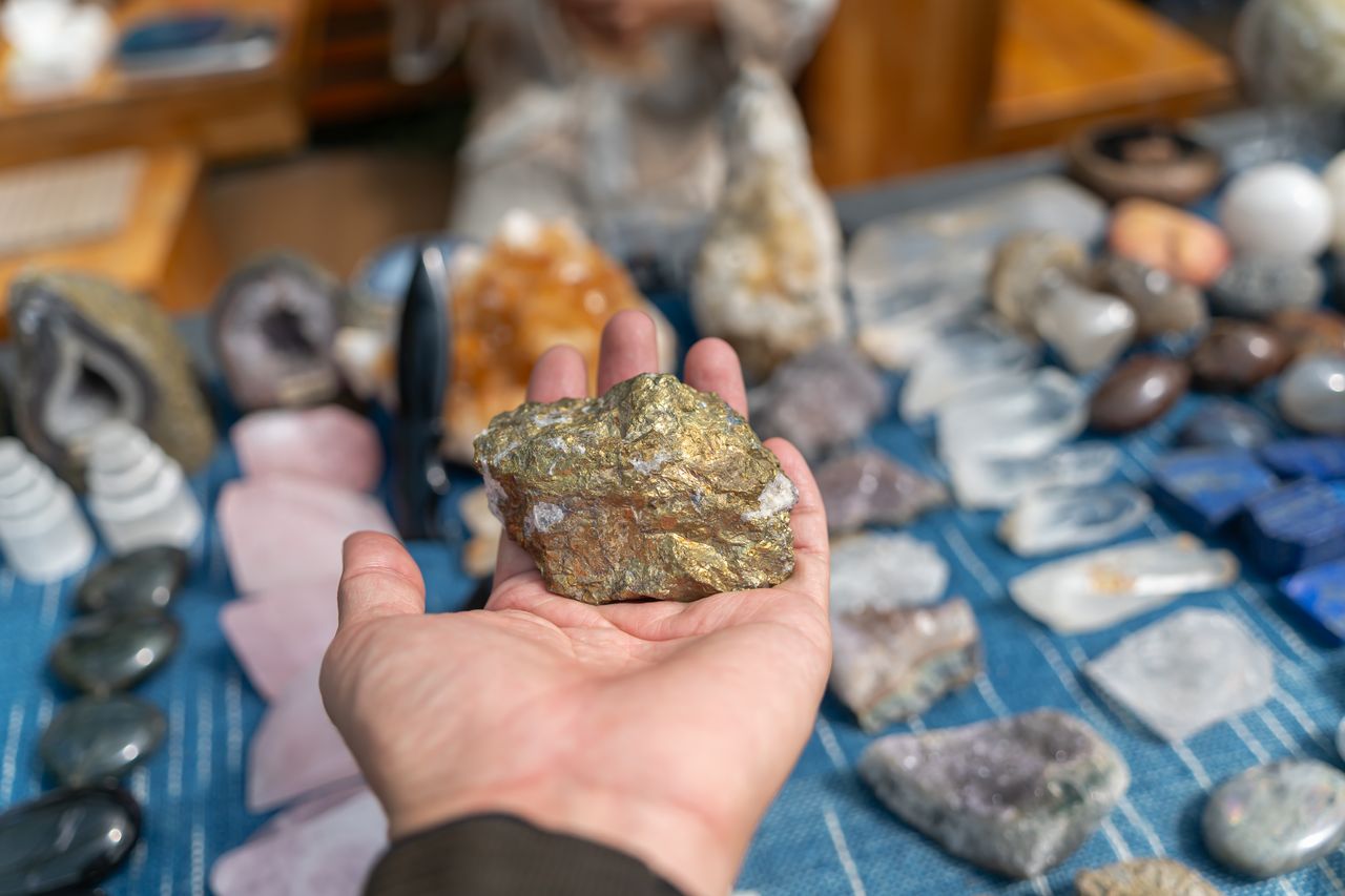 Hand displaying a raw mineral rock at a vibrant crystal market with various gems in the background.